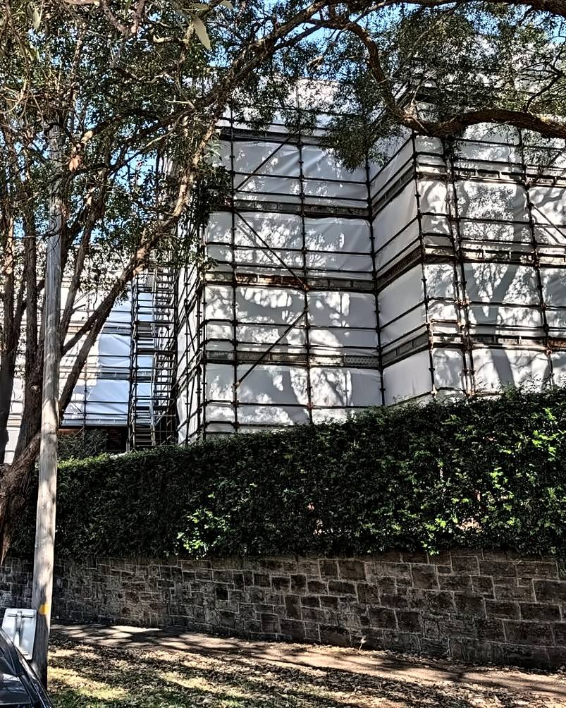 Monaflex-sheeted scaffold rising behind trees in Bellevue Hill